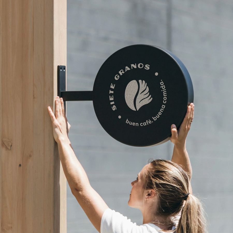 Persona colocando el letrero circular de Siete Granos en la pared de madera del local